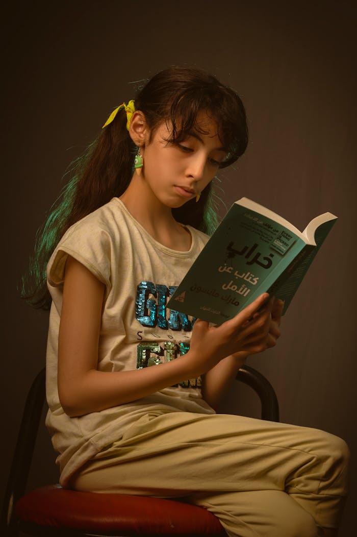 Thoughtful girl with long hair reads a book in a cozy studio setting.