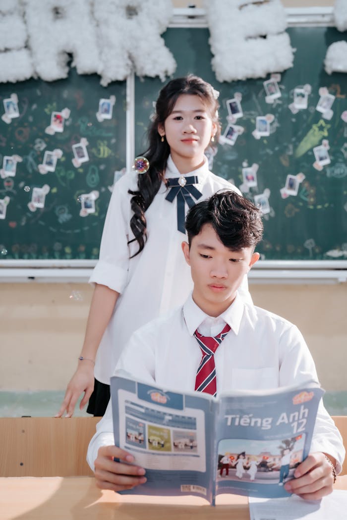 Two high school students studying with a textbook in a classroom setting.